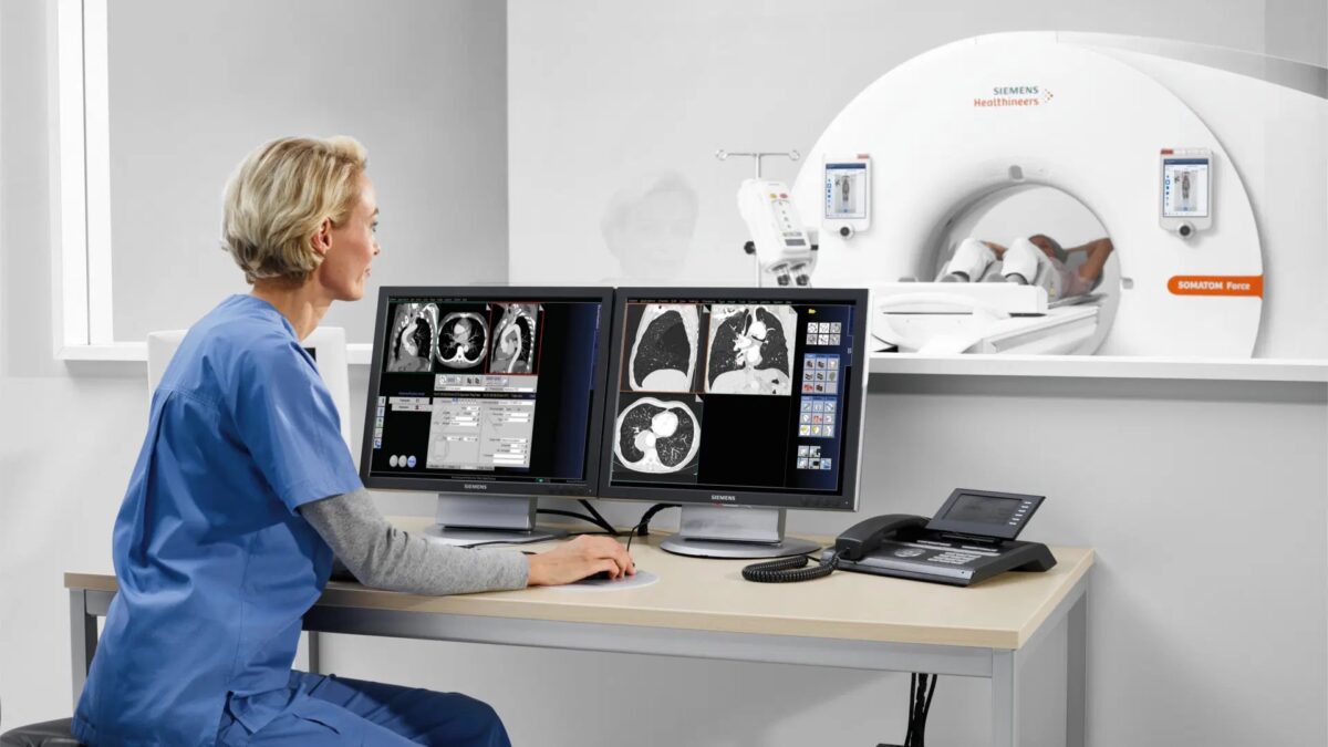doctor looking at a computer while a patient undergoes CT scanning